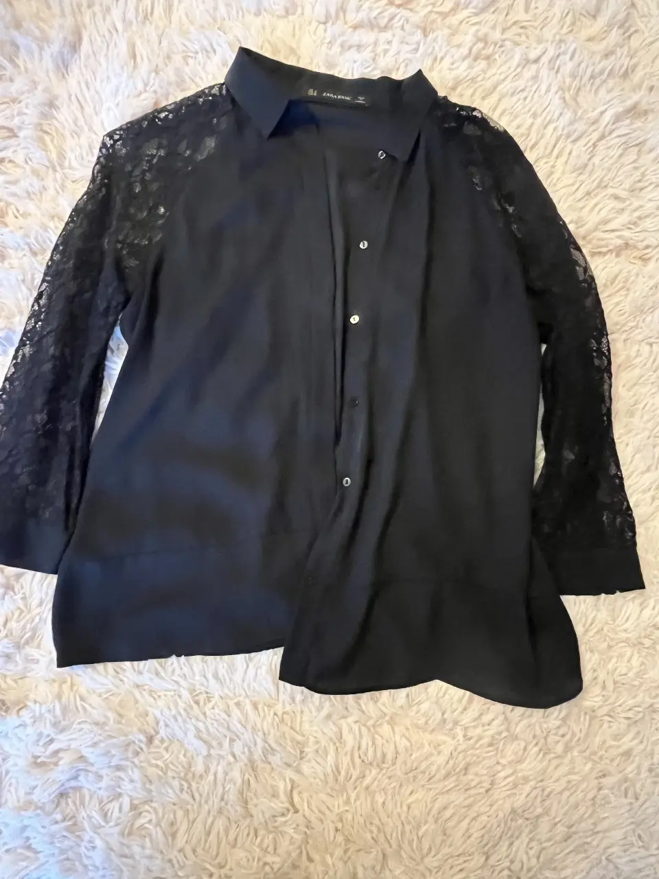 Blusa negra de manga larga con mangas de encaje. Ideal para un look elegante y sofisticado.