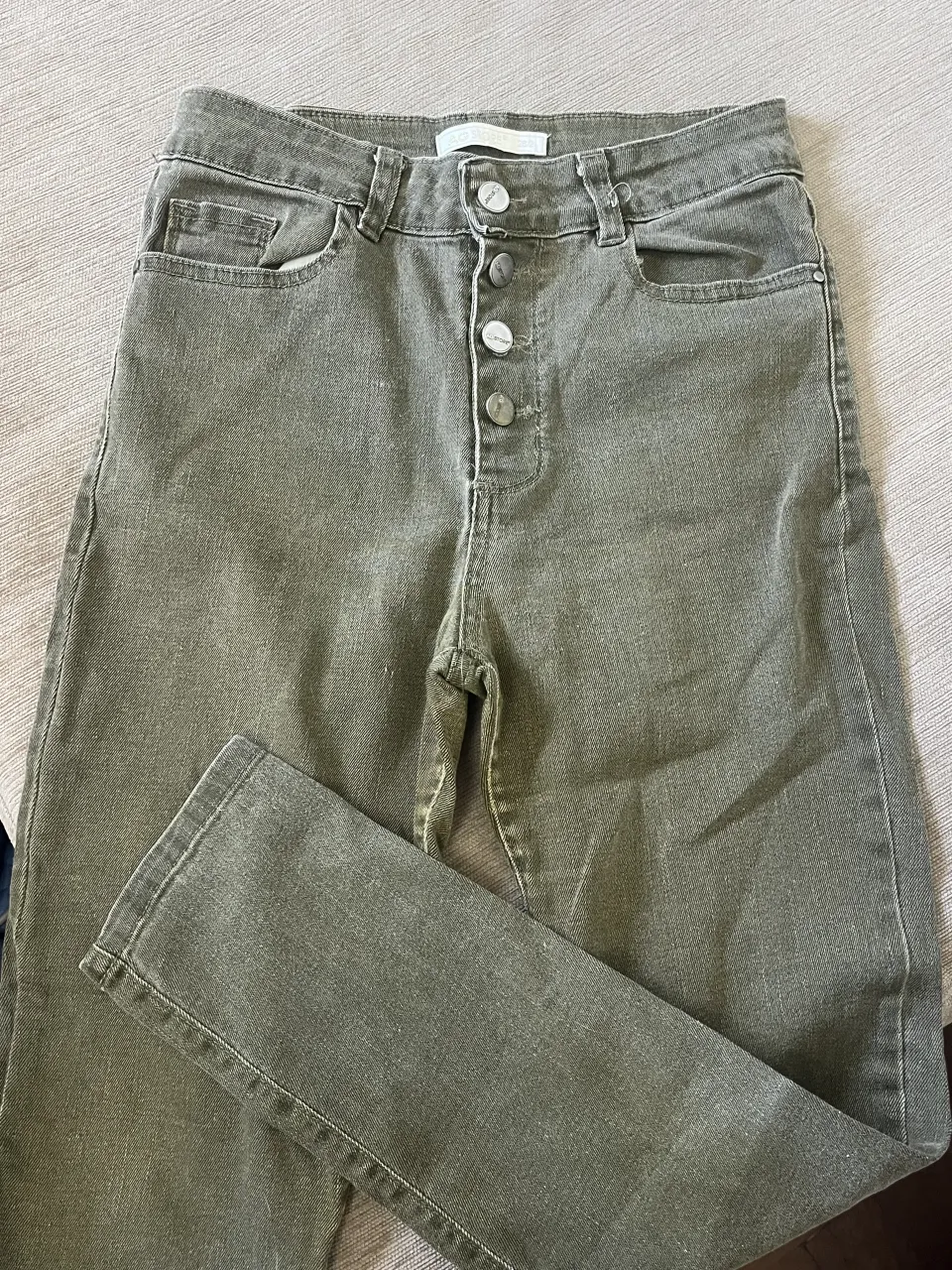 Jeans color verde militar con cinco botones al frente. Bolsillos delanteros y traseros.