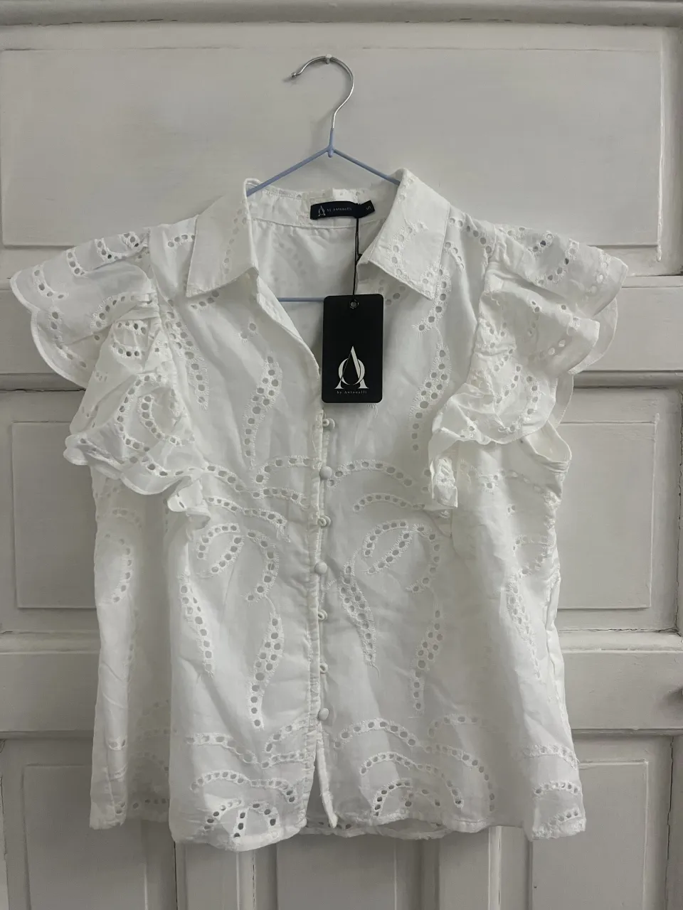 Blusa blanca con bordados y volados en las mangas. Posee cuello camisero y botones al frente.