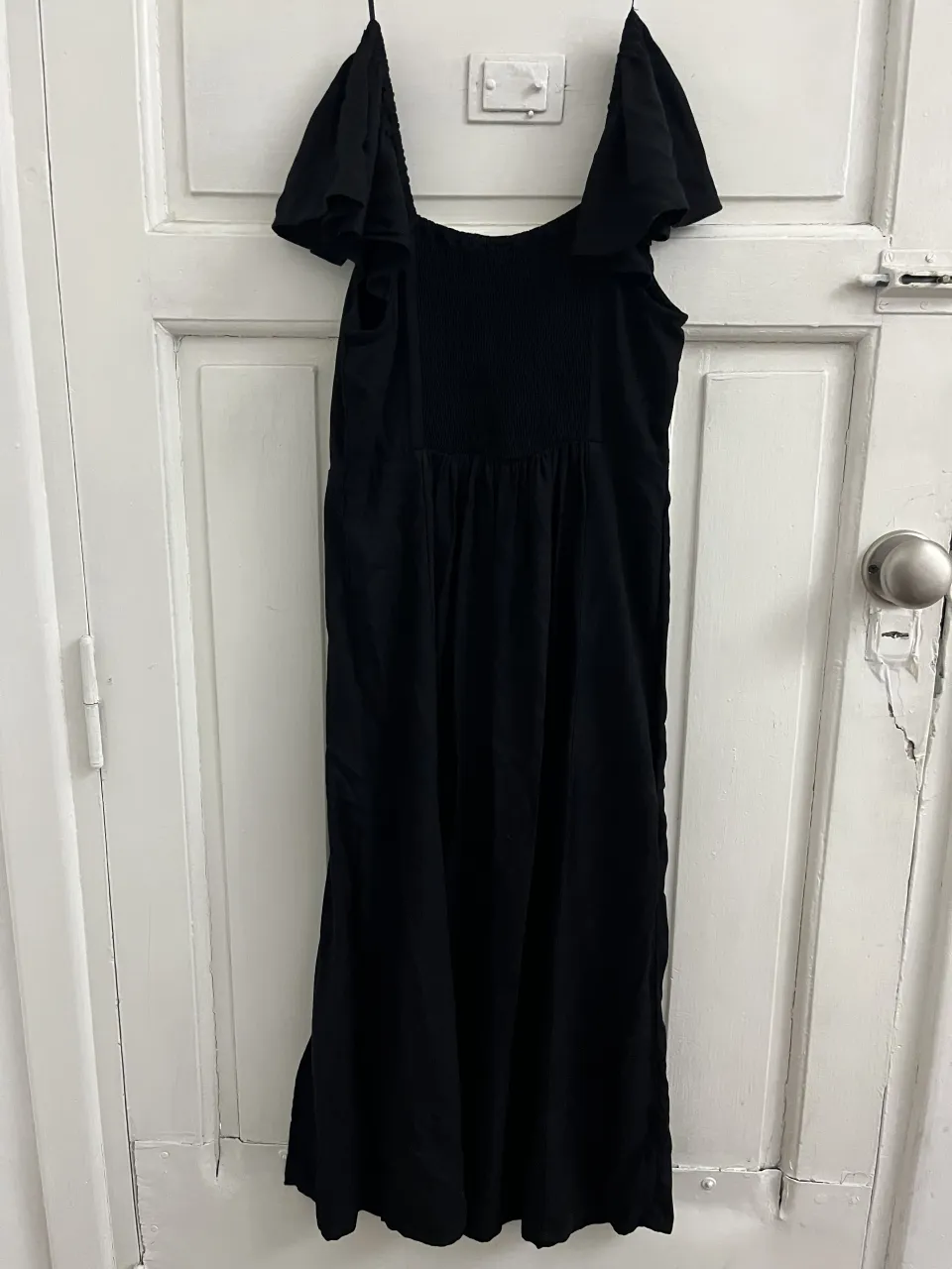 Vestido negro largo con breteles finos y volados en los hombros. Posee un elástico fruncido en la parte del busto y una abertura lateral en la falda.