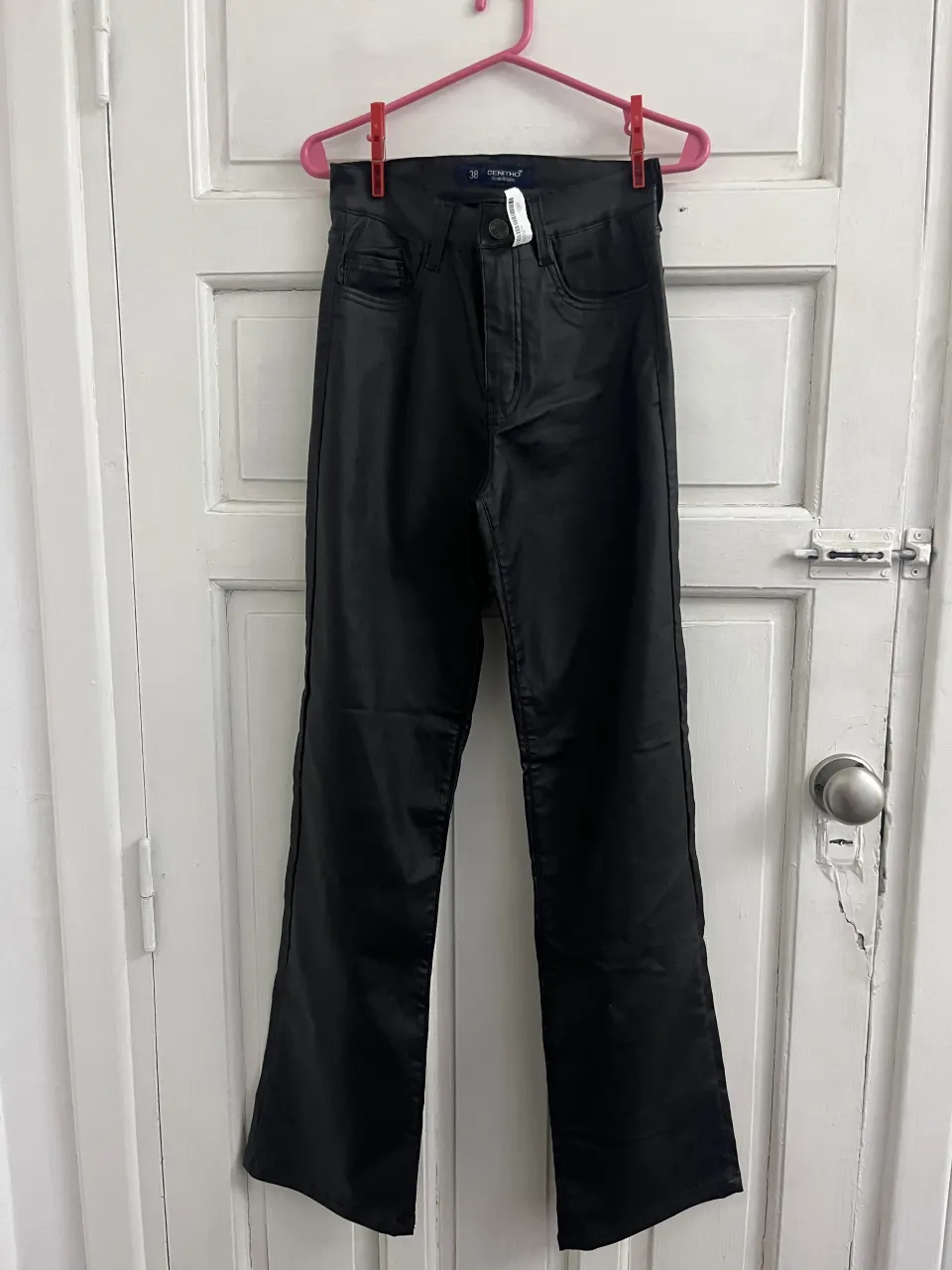 Pantalón negro de cuero sintético con cinco bolsillos y cierre.