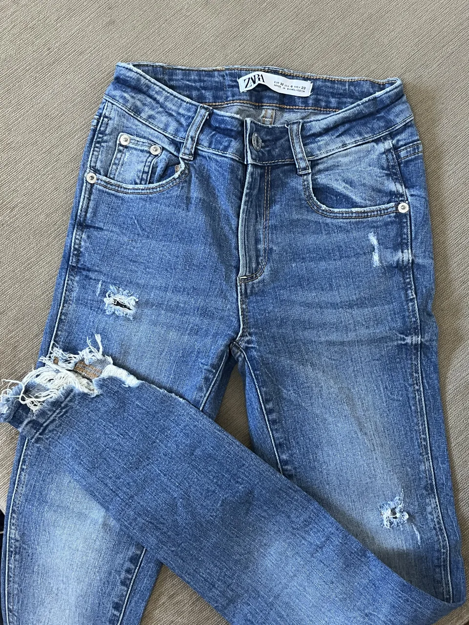 Jeans de tiro alto con roturas y detalles desgastados en la parte delantera y en los bajos. Tienen bolsillos delanteros y traseros.