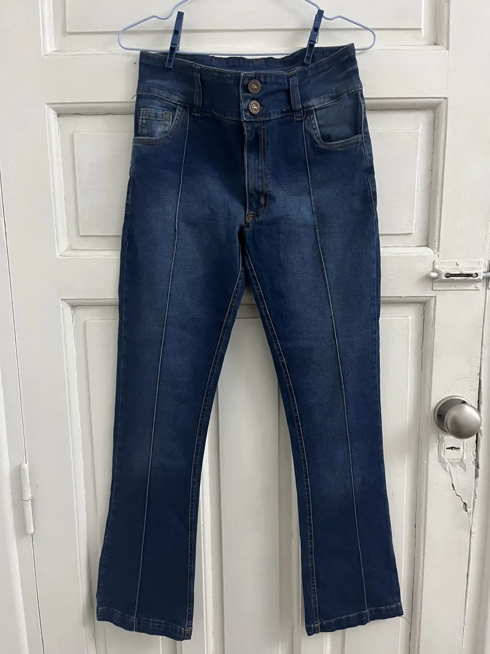 Jean azul oscuro con costuras verticales al frente y en la parte trasera. Posee dos botones en la cintura y bolsillos.