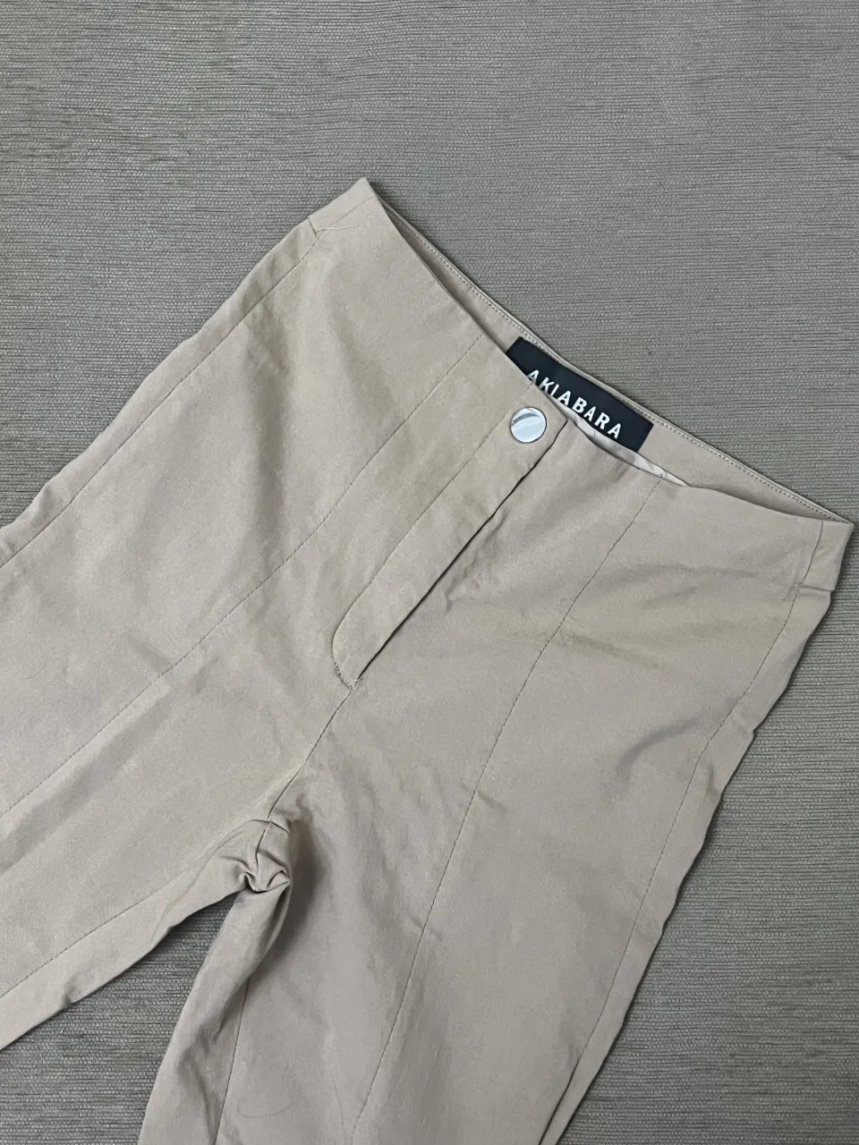 Pantalón color beige con pinzas delanteras y un botón en la cintura.