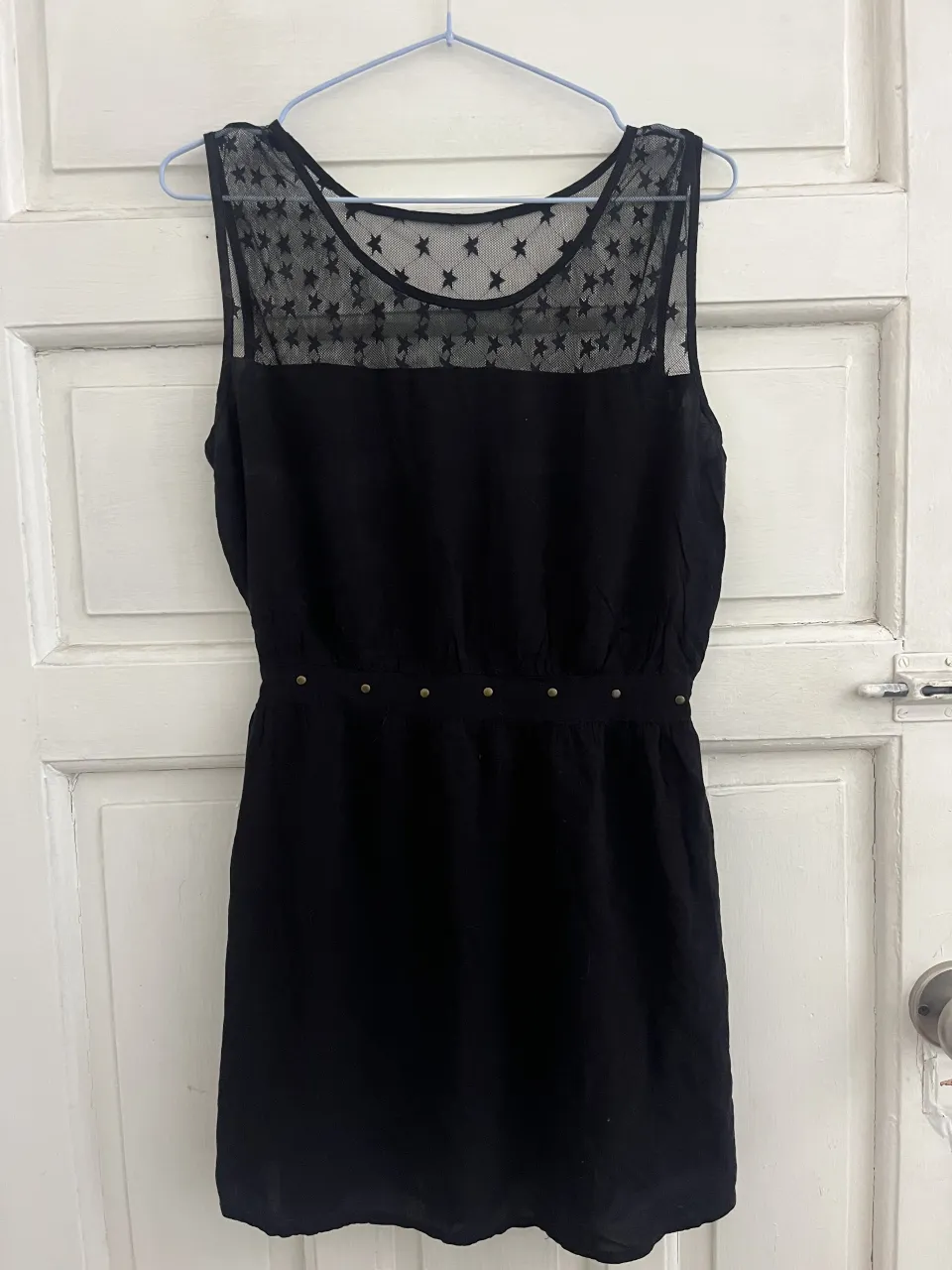 Vestido negro sin mangas con detalles de estrellas en la parte superior del escote. Cintura elastizada con detalles metálicos.