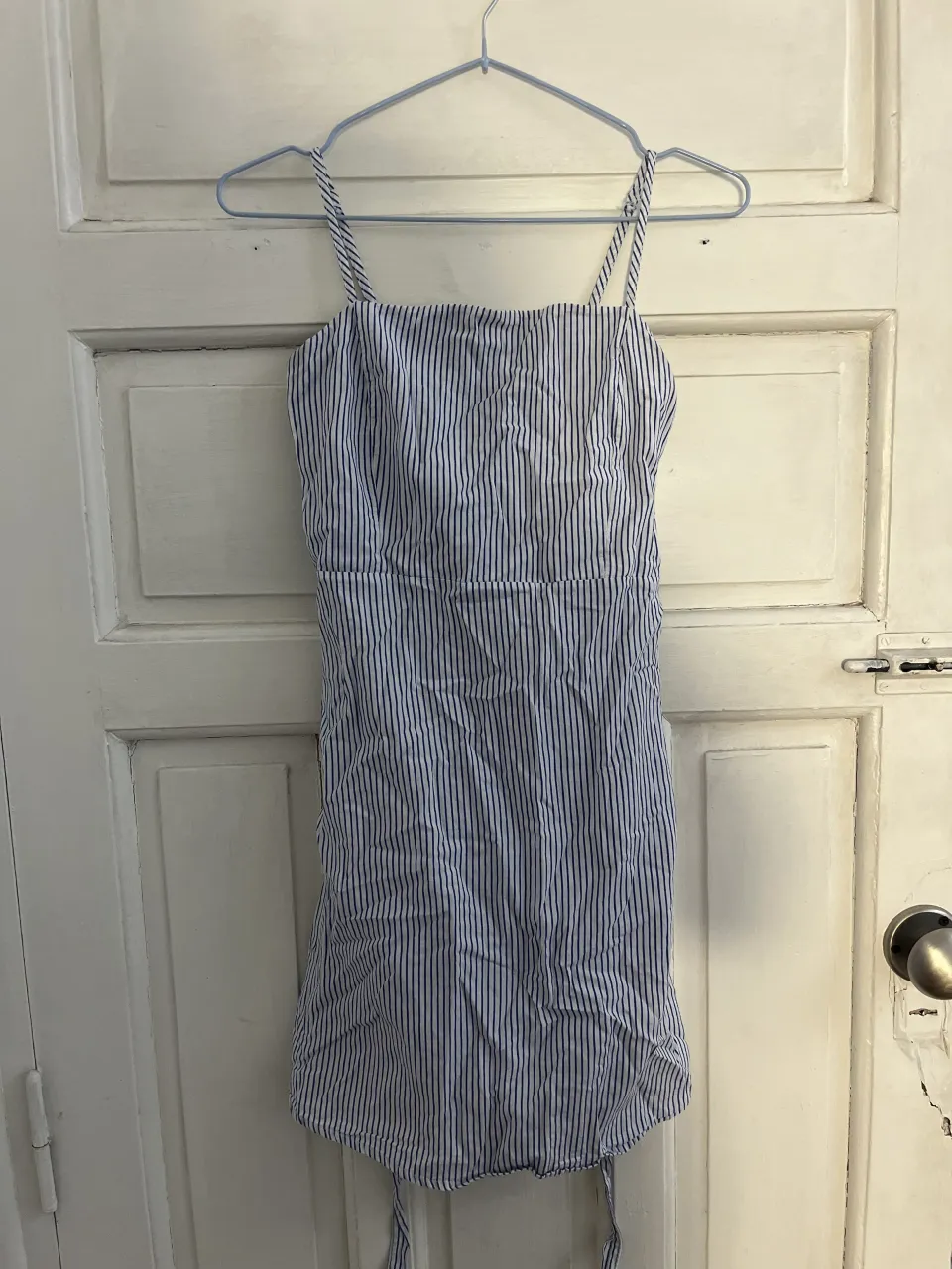 Vestido corto a rayas verticales blancas y azules. Breteles finos y escote cuadrado. Cintura con elástico y lazo para atar en la espalda.