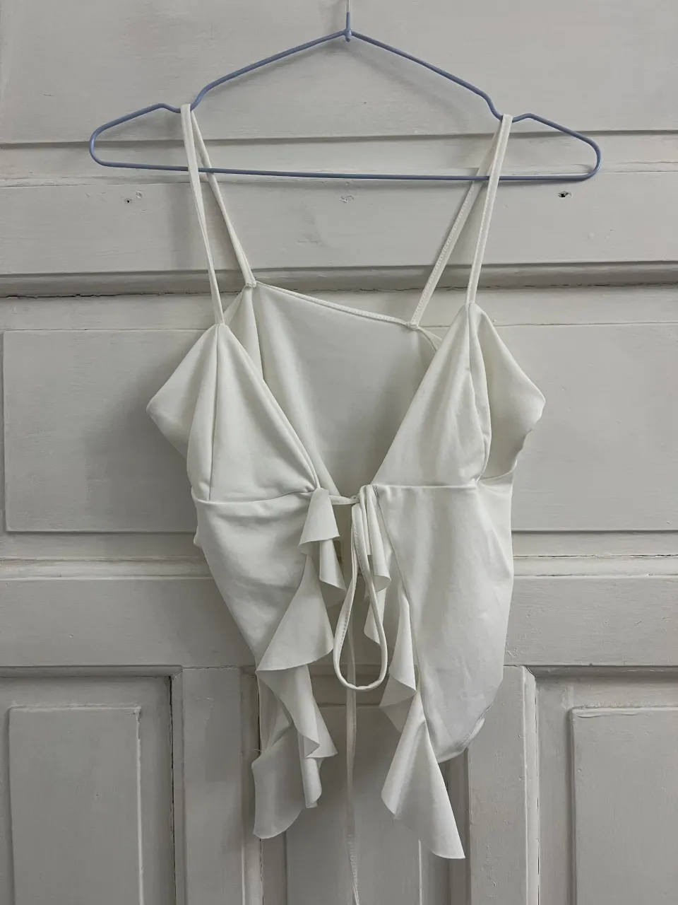 Top blanco con tiras finas y volados en la parte inferior. Posee un lazo para atar en la espalda.