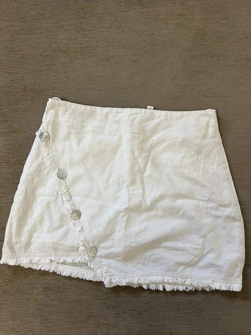 Pollera blanca con botones nacarados y detalles de flecos en el borde inferior y en el lateral.