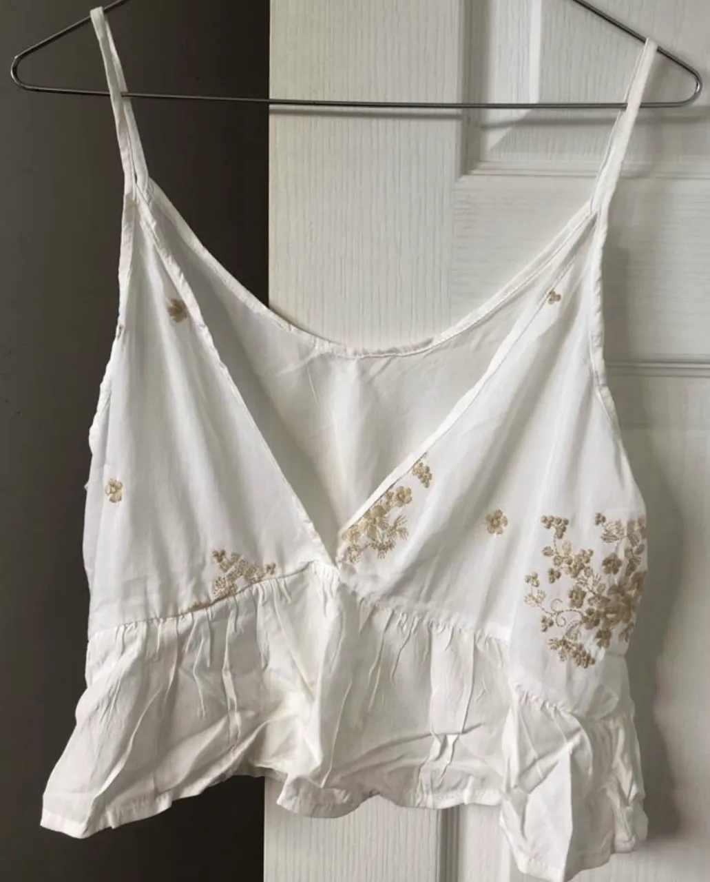 Top blanco con delicados bordados florales beige. Diseño con breteles finos y volado en la parte inferior. Ideal para un look fresco y femenino. Es nueva! medidas: axila a axila 45cm, largo 35cm