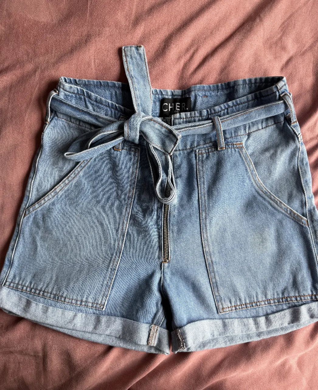 Shorts de jean tiro alto con cinto de tela y cierre metálico. Detalle de bolsillos amplios y dobladillo en la botamanga. Ideales para un look casual y canchero.