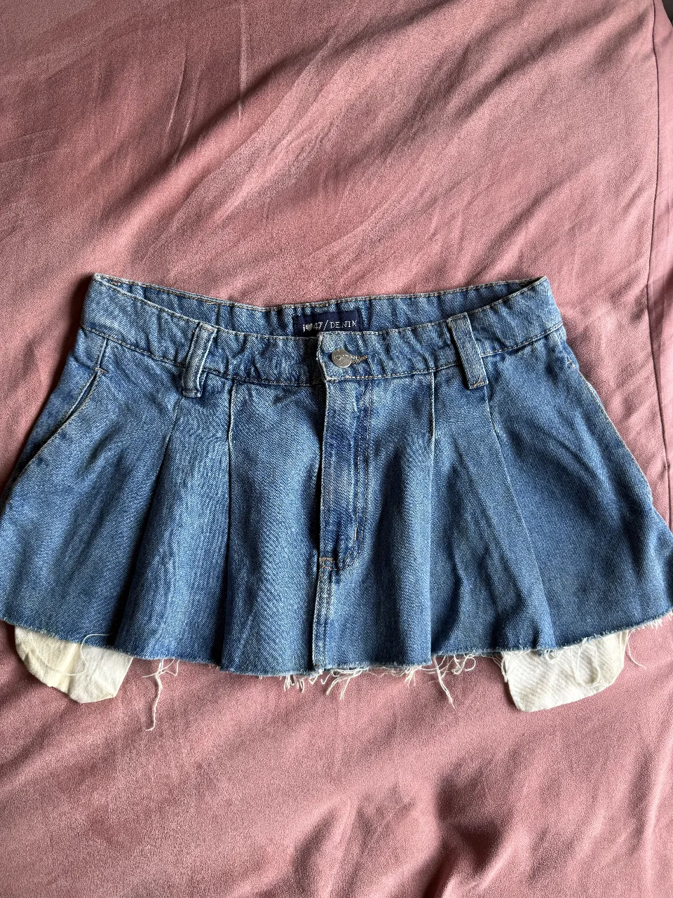 Pollera de jean tiro bajo, con detalles de roturas y fruncidos. Un diseño único y canchero, ideal para looks modernos y descontracturados. 