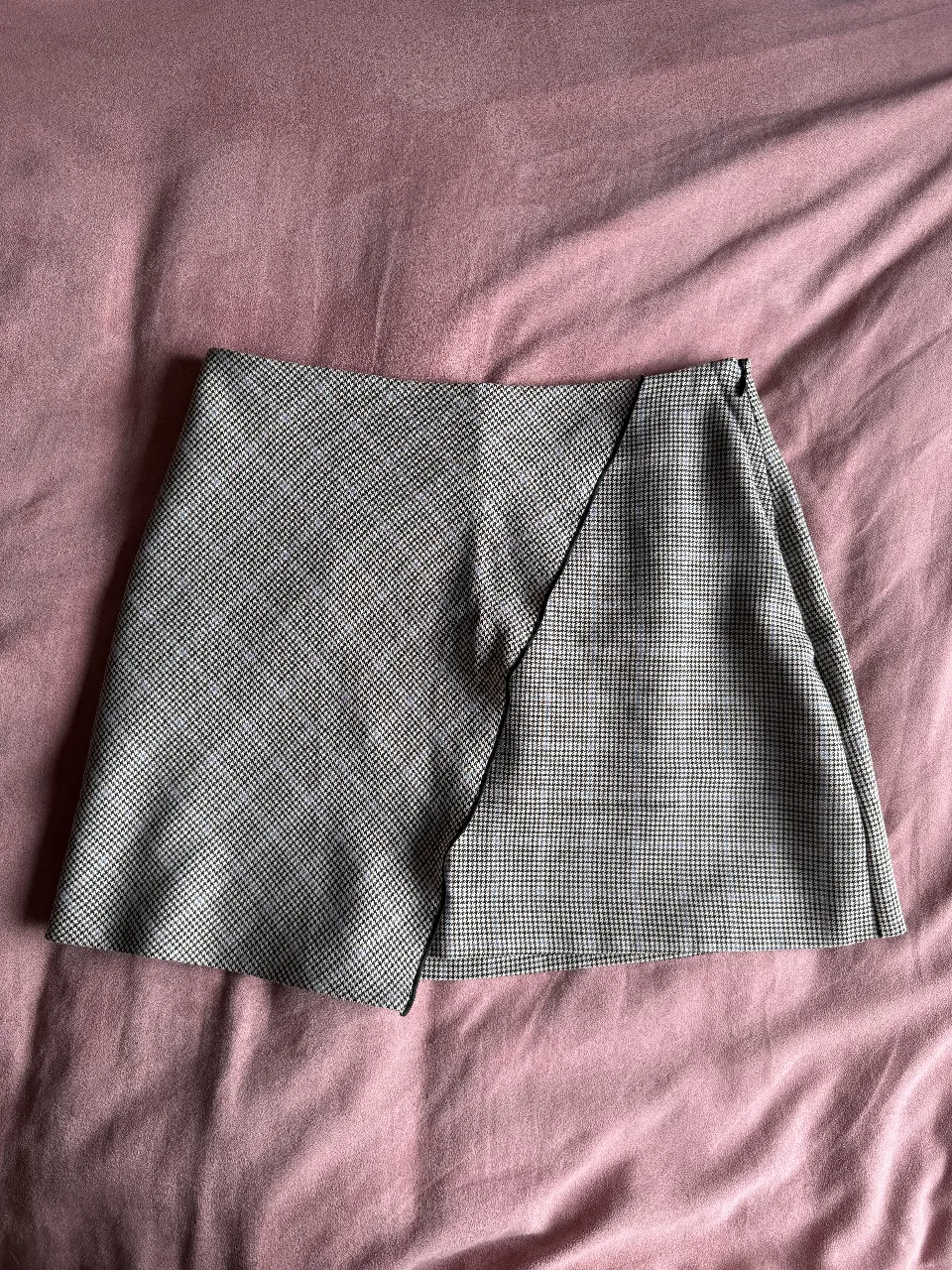 Pollera corta con un diseño asimétrico y estampado a cuadros pequeños en tonos grises y marrones. Ideal para un look casual o de oficina.