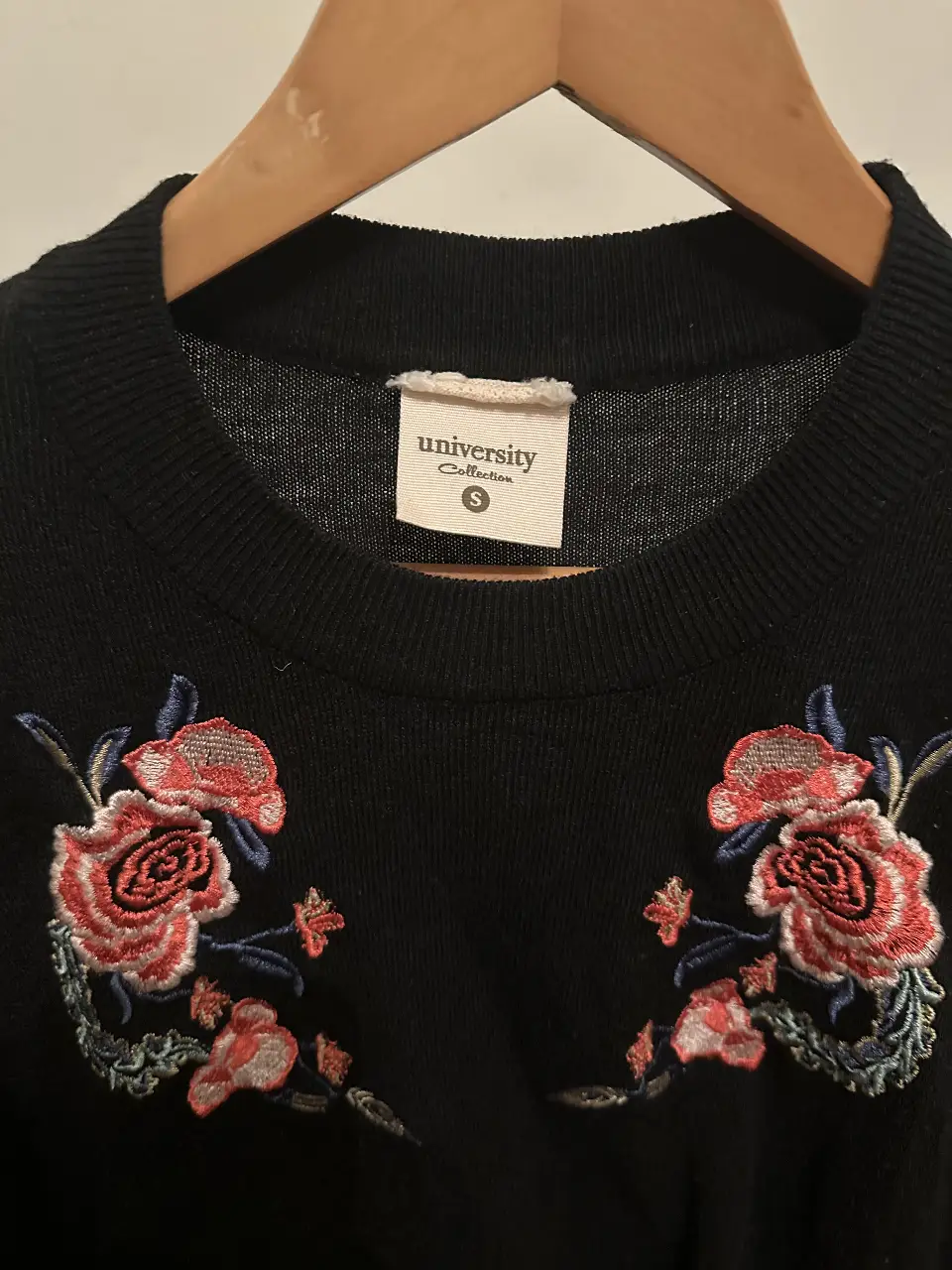 Sweater negro de la marca University Collection con bordado floral en rojo y azul. Talle S.