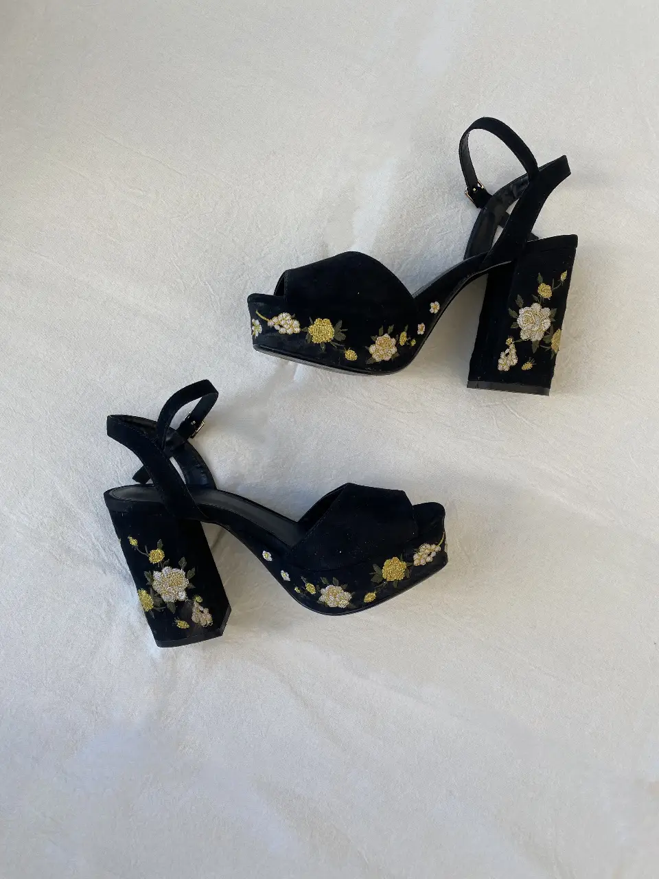 Sandalias de plataforma negras con bordado floral en tonos amarillos y blancos. Tiras finas en el tobillo y taco ancho. Ideales para darle un toque elegante y moderno a tus looks de fiesta.