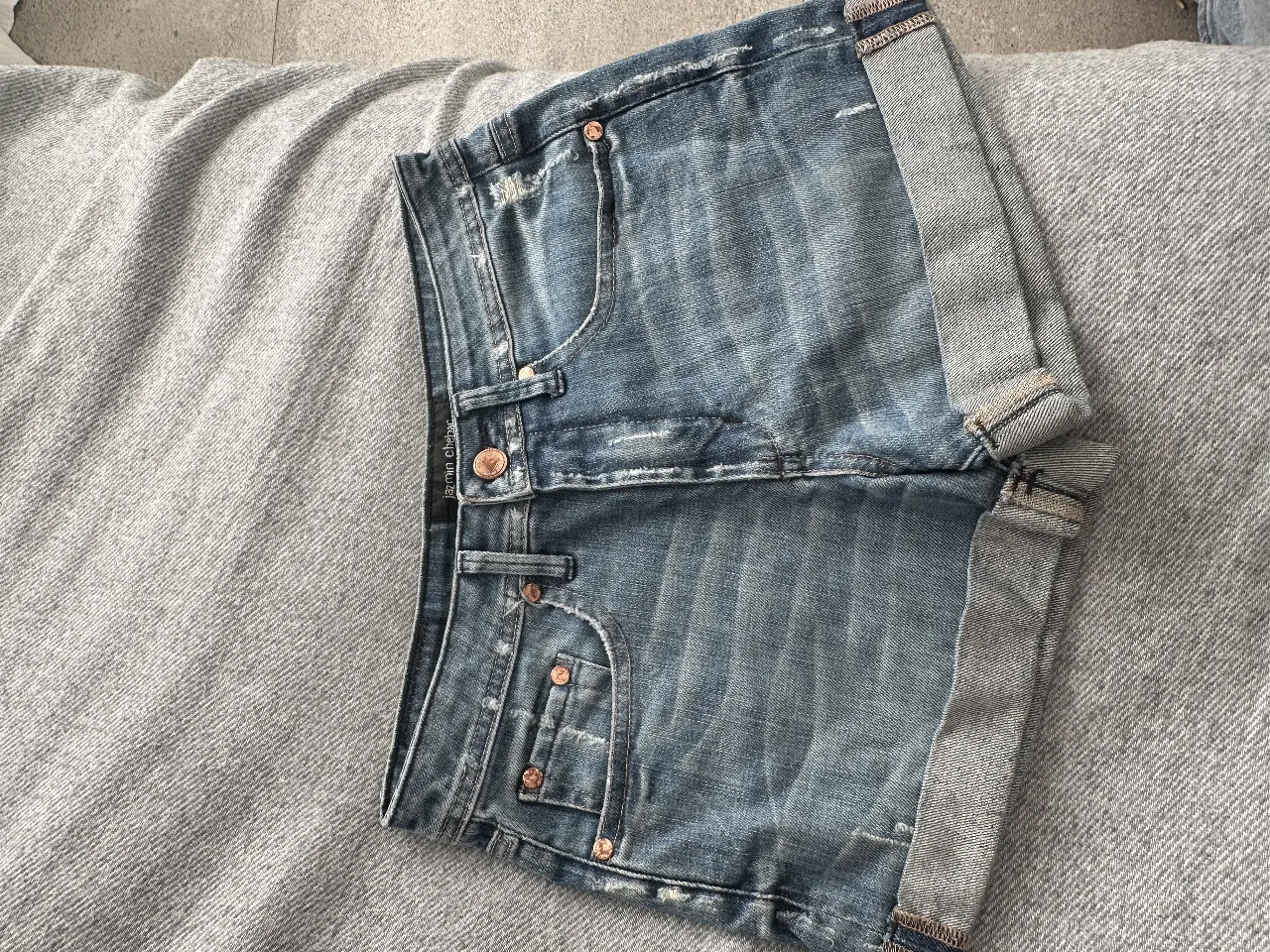 Short de jean azul con detalles de desgaste y dobladillo en los bordes. Tiro medio, ideal para un look casual y moderno.