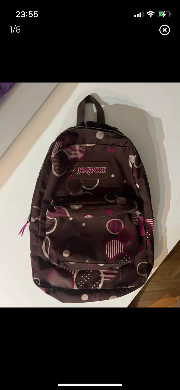 Mochila JanSport con estampado de círculos en tonos marrones y violetas. Ideal para uso diario, con bolsillo frontal y detalles de la marca.
