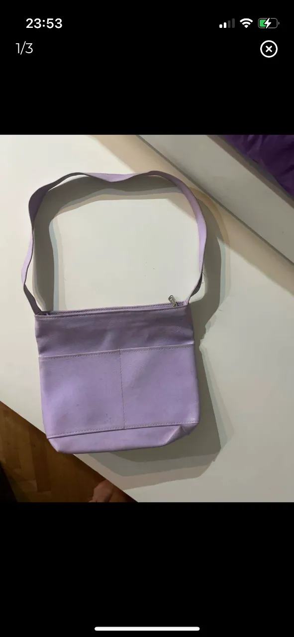 Cartera bandolera de color lila, con un diseño simple y elegante. Cuenta con un compartimento principal con cierre y una correa ajustable para llevarla al hombro. Ideal para un look casual y moderno.