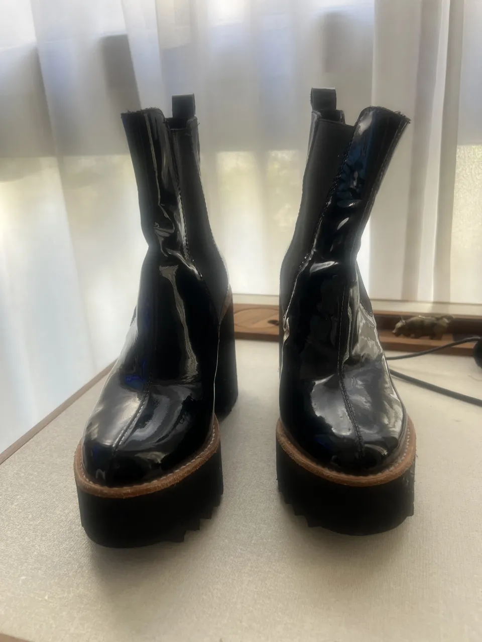 Botas negras de charol con plataforma y taco grueso. Tienen elástico a los costados y tiras en la parte superior trasera.