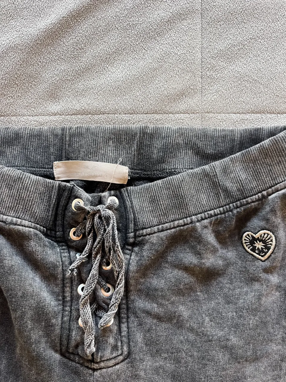 Pantalón de algodón gris con efecto desgastado y cordones en la cintura. Posee un pequeño bordado de corazón en el lateral.