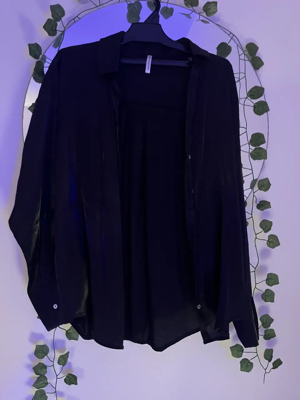 Camisa negra de manga larga, con cuello, los botones no llegan arriba del todo es un poco escotada. Tela con un poco de brillo y muy poco transparente. 