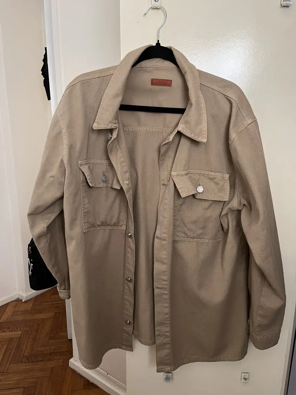 Camisa shacket de gabardina color beige, con dos bolsillos delanteros con solapa y botones. Cuello camisero y cierre frontal con botones.