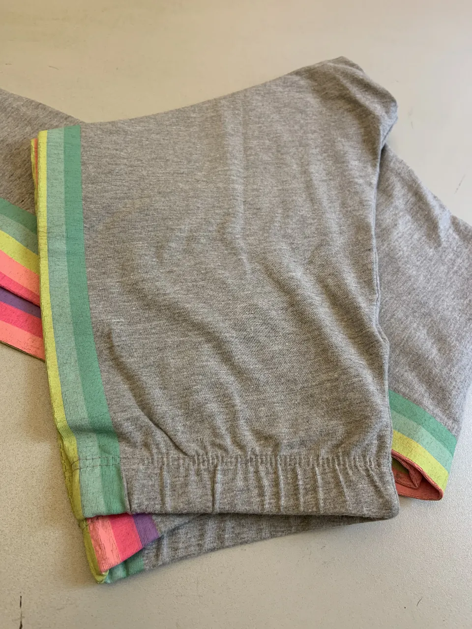 calza gris con detalles de franjas arcoíris en los laterales. Ideal para un look cómodo y moderno.