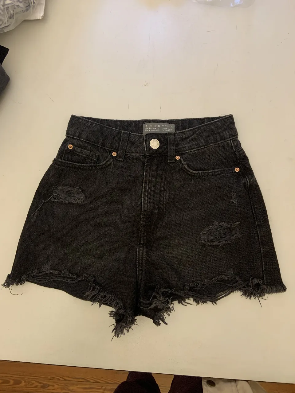 Short de jean negro con roturas y flecos en el borde. Tiro alto, ideal para un look casual y moderno.