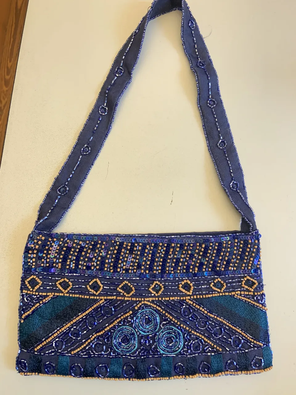 Cartera Express de mano azul con detalles bordados y lentejuelas. Diseño artesanal con correa para colgar al hombro. Ideal para eventos especiales o para darle un toque único a tu look. Viene con bolsa de mostacillas de repuesto. Cierre con imán. Sin uso. 24x13. Correa 60 cm. 