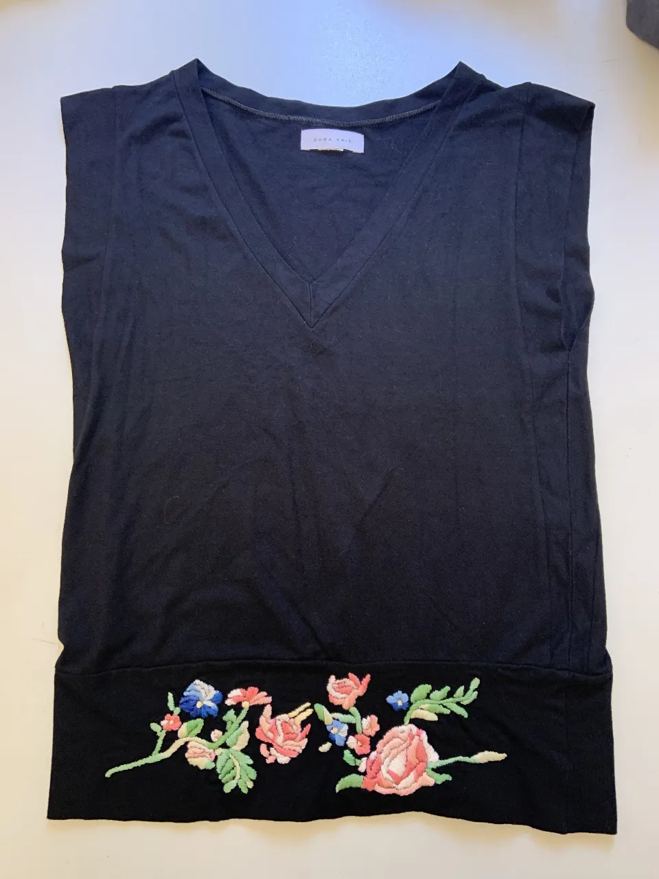 Musculosa negra de mujer con cuello en V . Manga japonesa y bordado floral en la parte inferior. Ideal para un look casual y fresco.
