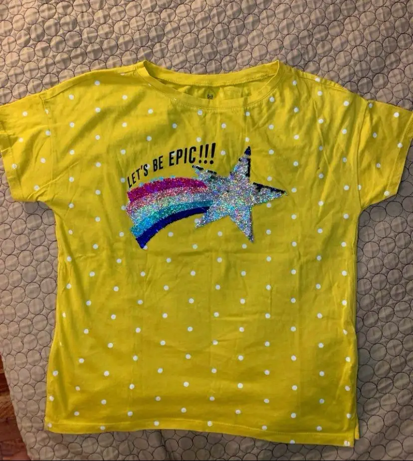 Remera amarilla con lunares blancos y estampado "Let's be epic!!!" con una estrella y un arcoíris de lentejuelas. Ideal para un look casual y divertido.