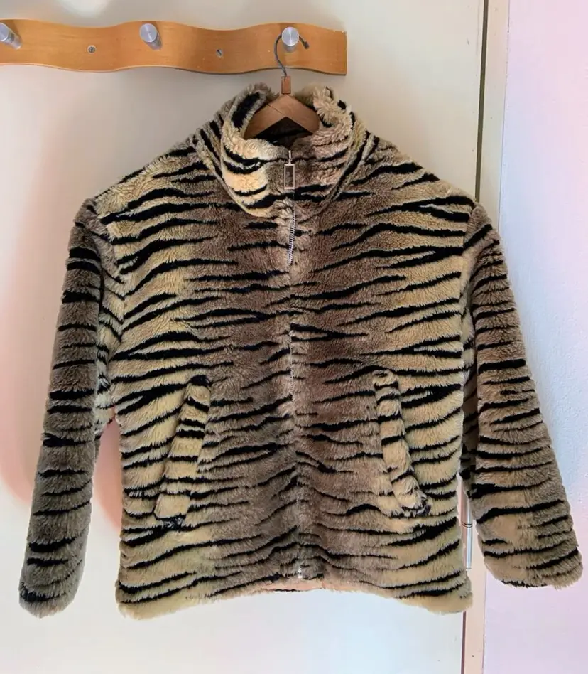 Campera de abrigo con estampado de tigre, con cierre frontal y bolsillos. Ideal para un look audaz y moderno. Tiene descosido el interior de un bolsillo, se puede remendar. Por fuera está impecable. 