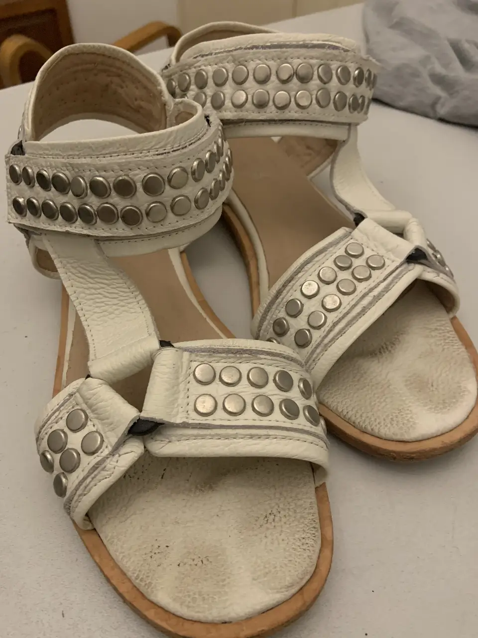 Sandalias blancas con detalles de tachas plateadas. Diseño moderno y cómodo, ideales para un look casual y con estilo.