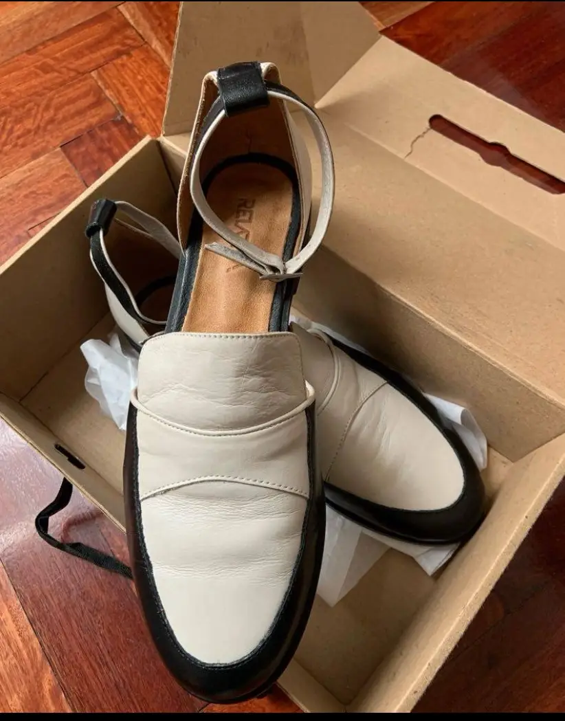 zapatos tipo mocasín con pulsera en color marfil y negro. Diseño elegante y moderno, ideales para un look casual o de trabajo.