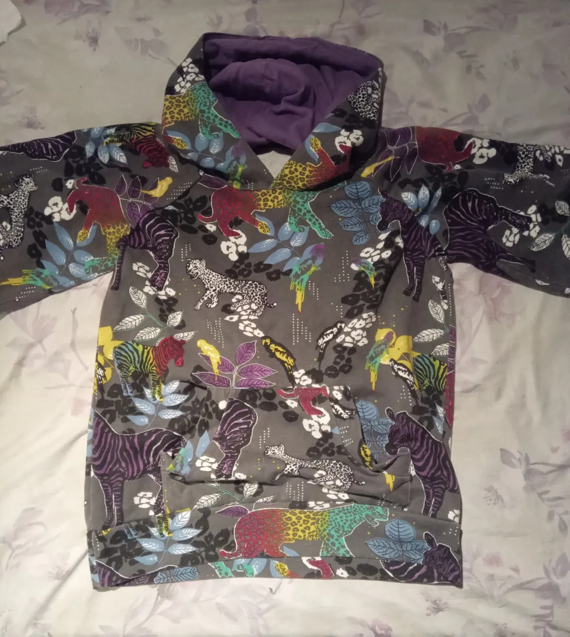 Buzo gris con capucha y estampa de animales salvajes y hojas en varios colores. Posee bolsillo canguro al frente.