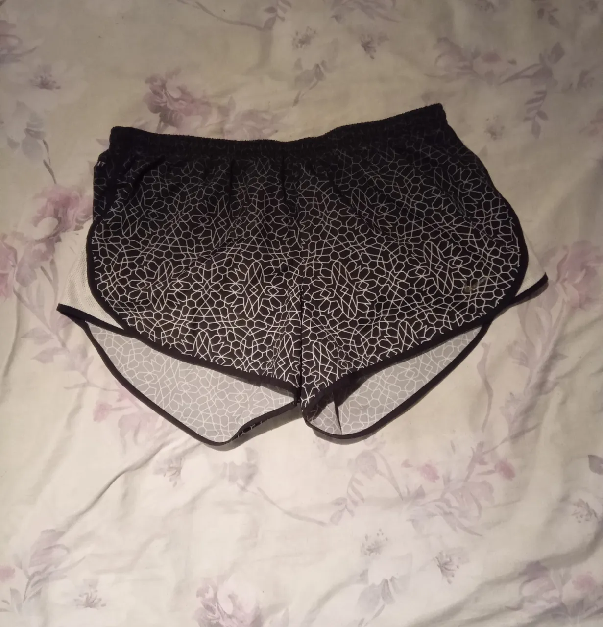 Shorts deportivos negros con estampado geométrico blanco y detalles laterales blancos.