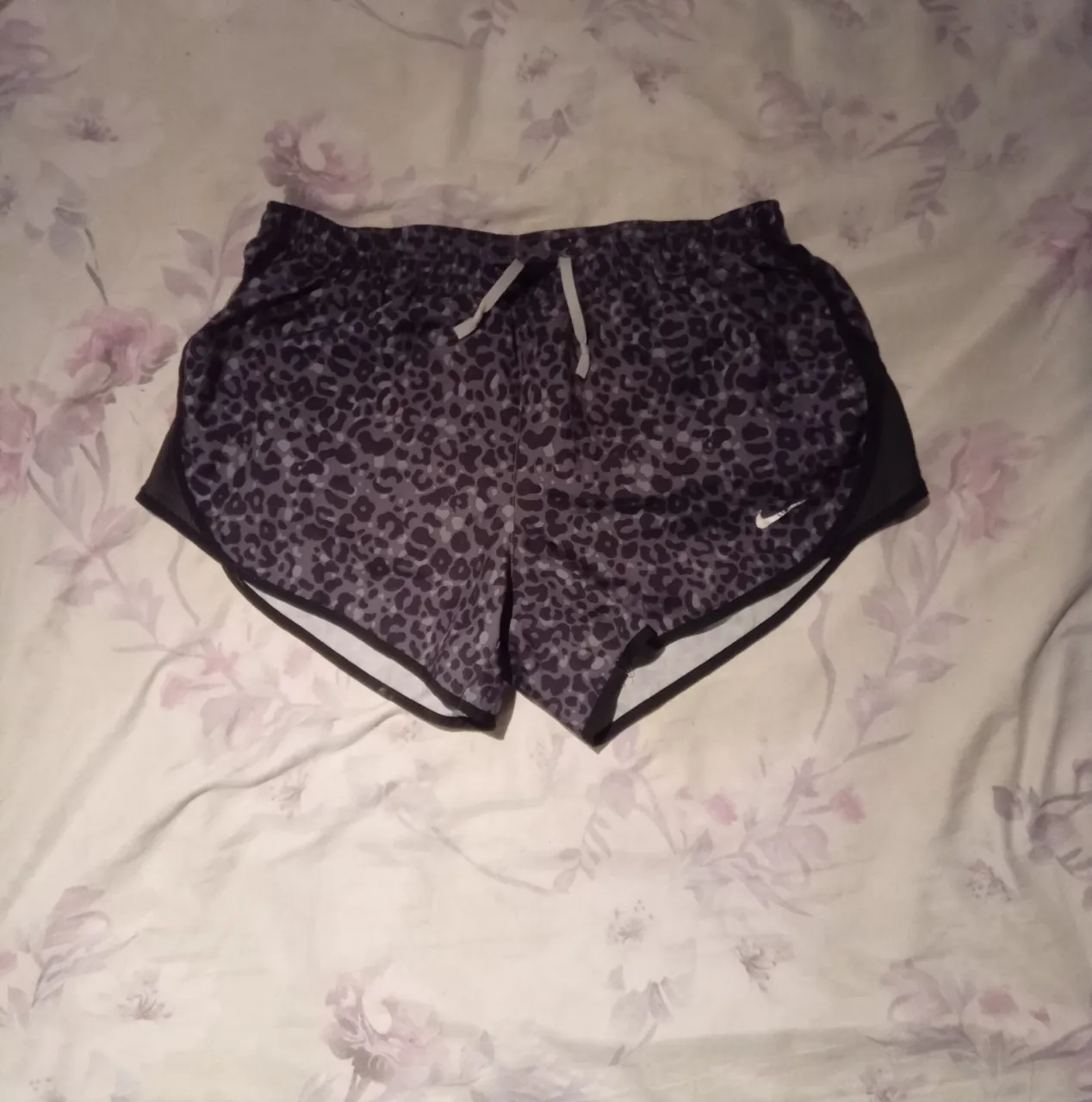 Shorts deportivos con estampa animal print en tonos grises y negros. Posee cordón de ajuste en la cintura y un pequeño bolsillo con cierre en la parte trasera. Tiene un detalle de rotura en la tela en la parte delantera.