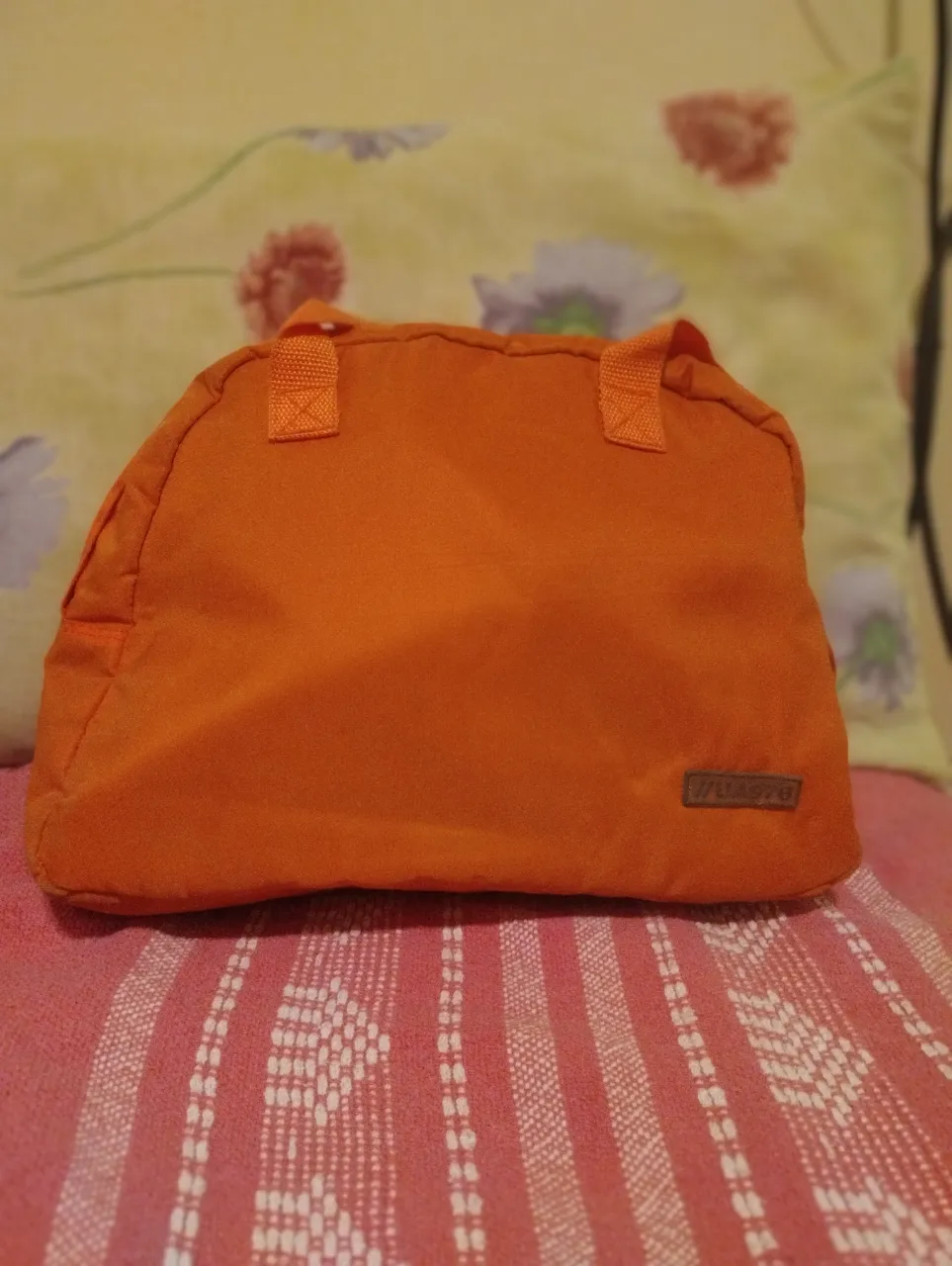 Bolso deportivo naranja con dos manijas cortas y una correa larga desmontable. Tiene un bolsillo interior con cierre.