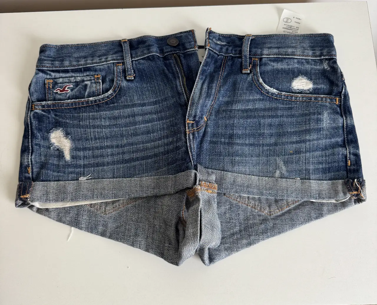 Short de jean Hollister azul, tiro medio, con detalles de roturas y dobladillo en el borde. Talle 28.