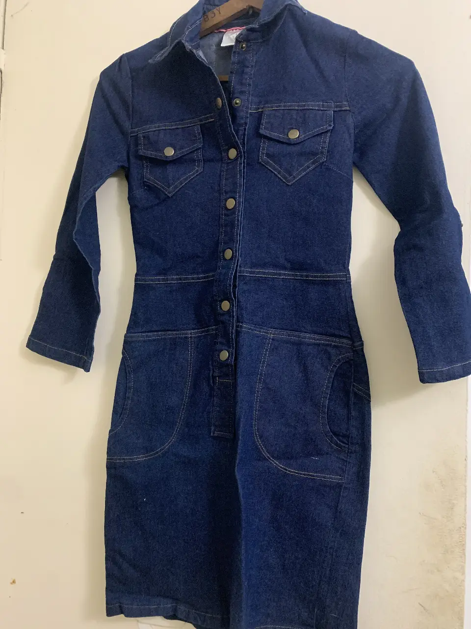 Vestido mini de jean azul, con mangas 3/4 y botones delanteros. Posee bolsillos delanteros y un diseño clásico y versátil, ideal para un look casual con un toque retro.