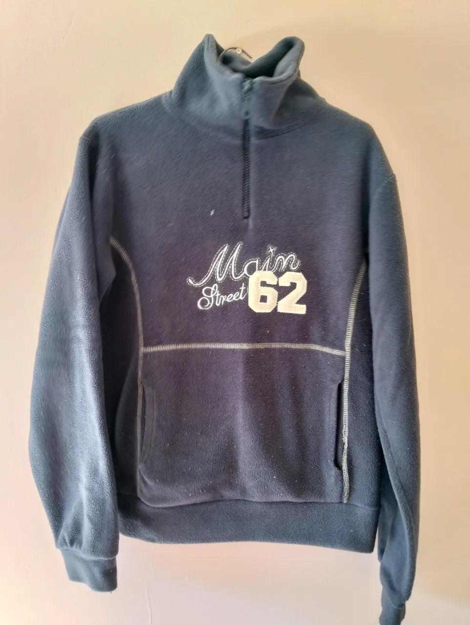 Buzo polar gris 
 marino con cierre y cuello alto. Diseño con estampado "Main Street 62" en blanco. Ideal para un look casual y abrigado.