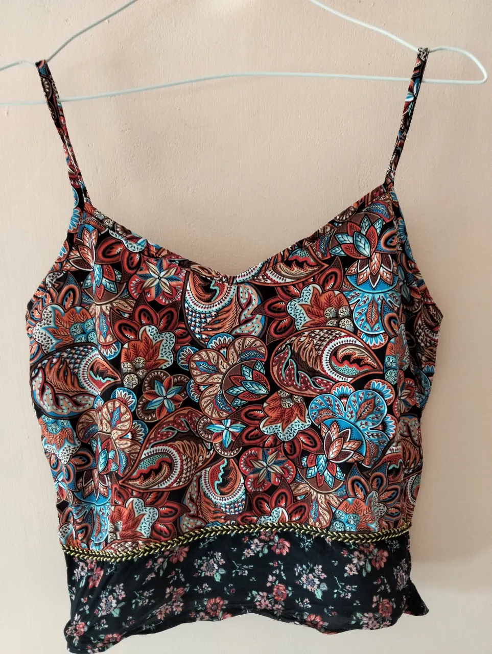 Top de mujer con estampado floral y paisley en tonos vibrantes. Diseño con tirantes finos y detalle de borde dorado en la cintura. Ideal para un look bohemio y fresco.