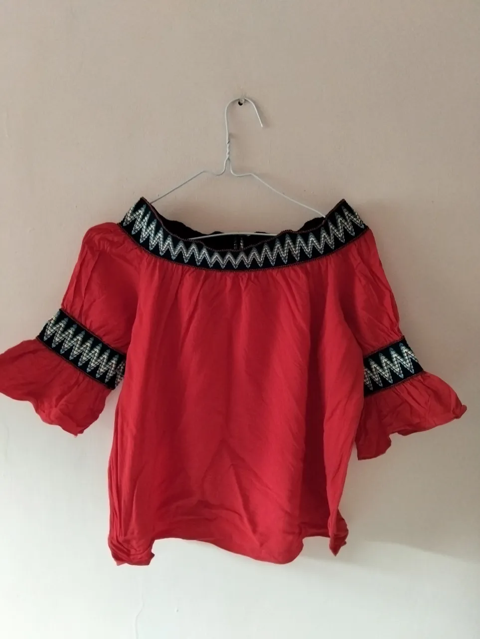 Blusa roja con detalles bordados en negro y blanco en el cuello y mangas. Estilo off-shoulder, ideal para un look fresco y moderno.