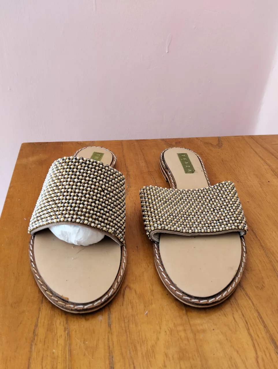 Sandalias planas doradas con apliques de strass y perlas, ideales para un look elegante y cómodo. Perfectas para el verano y salidas casuales.
