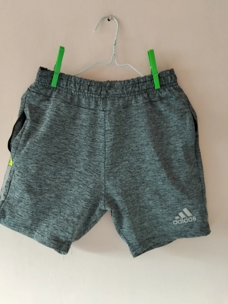 Short deportivo Adidas para hombre, color gris con detalles en amarillo y blanco. Ideal para actividades físicas.