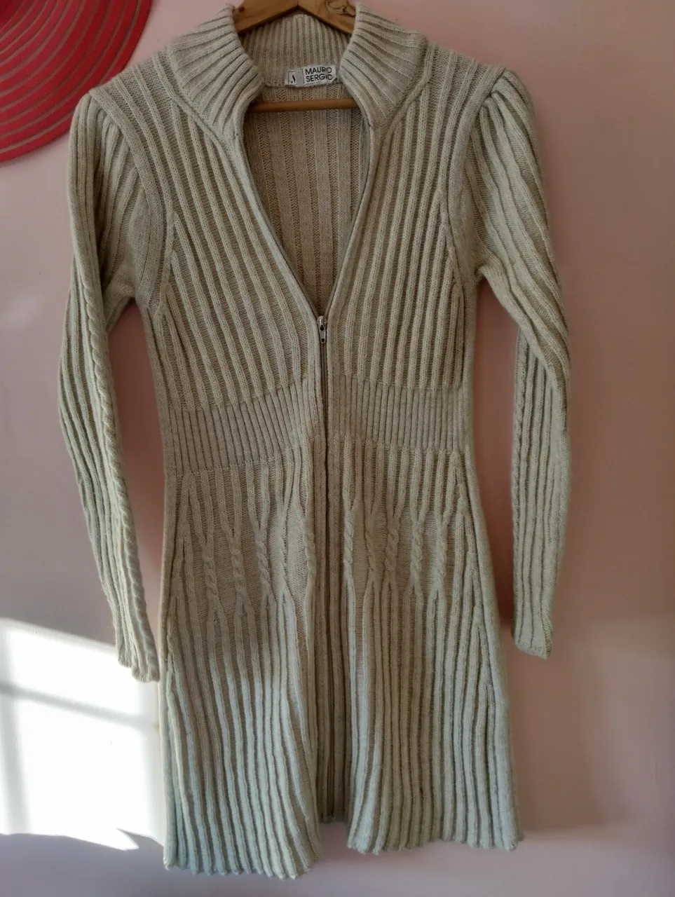 Cardigan largo tejido de lana color crudo, con cierre y cuello alto. Estilo casual y abrigado, ideal para el invierno.