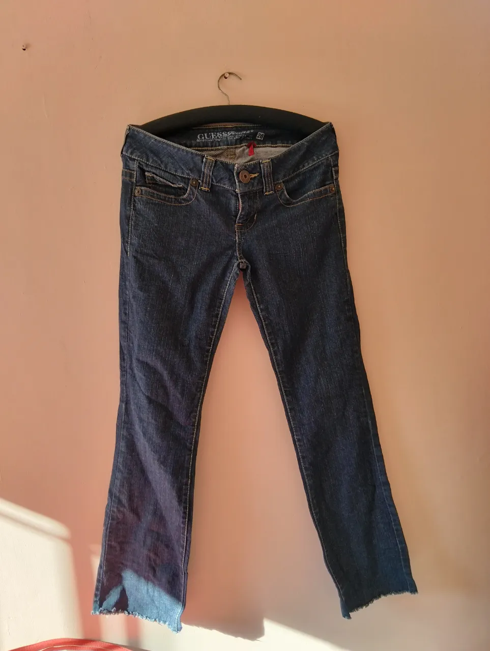 Jeans Guess de mujer, tiro bajo, corte bootcut, color azul oscuro. Con detalles de costuras en color ocre y el logo de la marca en los bolsillos traseros. Talle 28.
