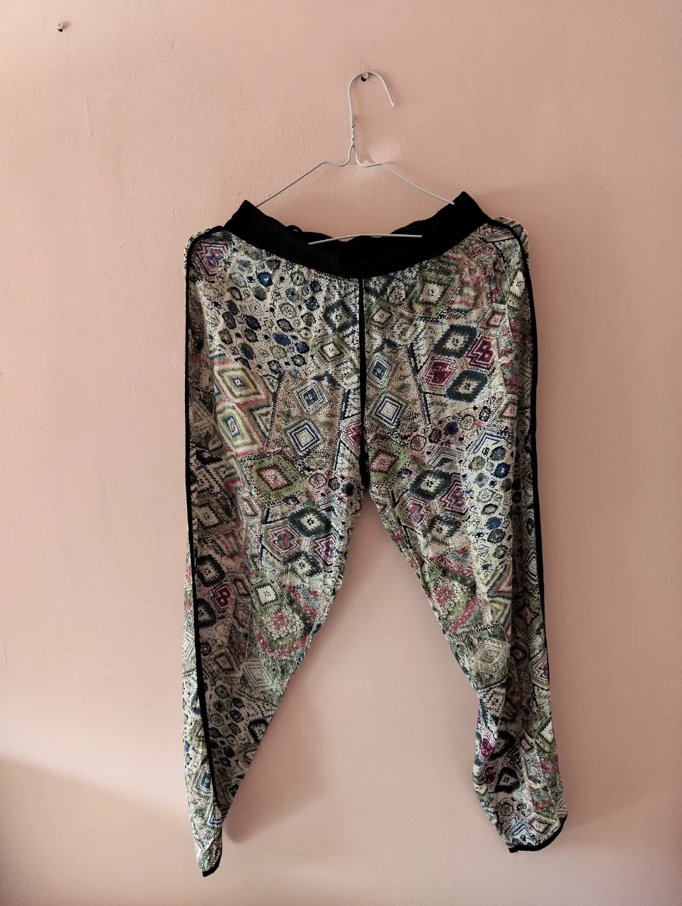 Pantalón suelto de mujer con estampado geométrico en tonos vibrantes. Cintura negra elástica y detalles en negro en los laterales. Ideal para un look boho-chic y cómodo.
