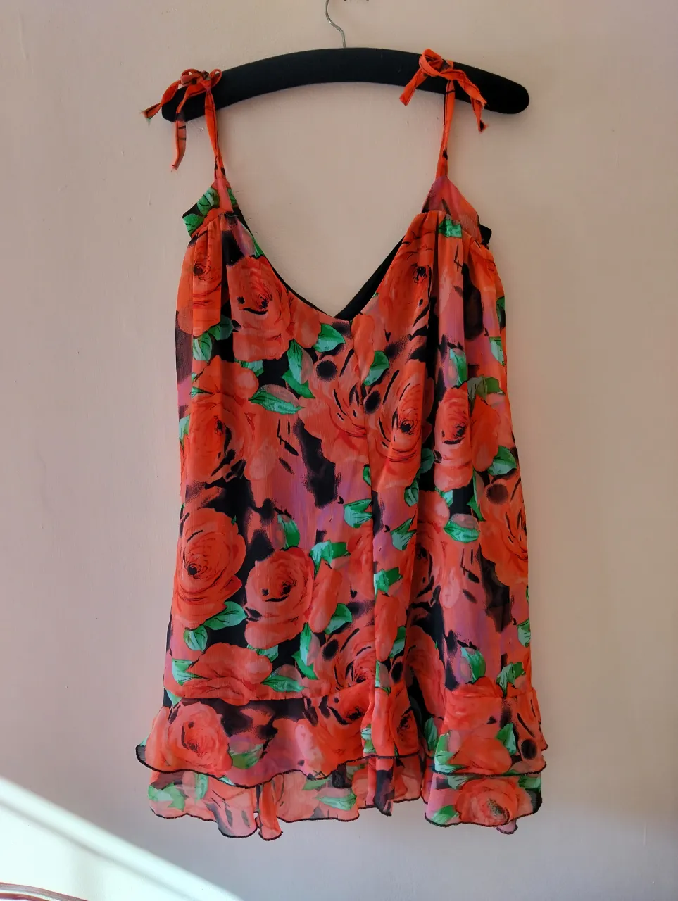 Vestido mini de mujer con estampado floral en tonos rojos y negros. Ideal para una salida o fiesta, este vestido sin mangas presenta un diseño con volados en el bajo y tirantes finos. Perfecto para lucir fresca y con estilo en verano.