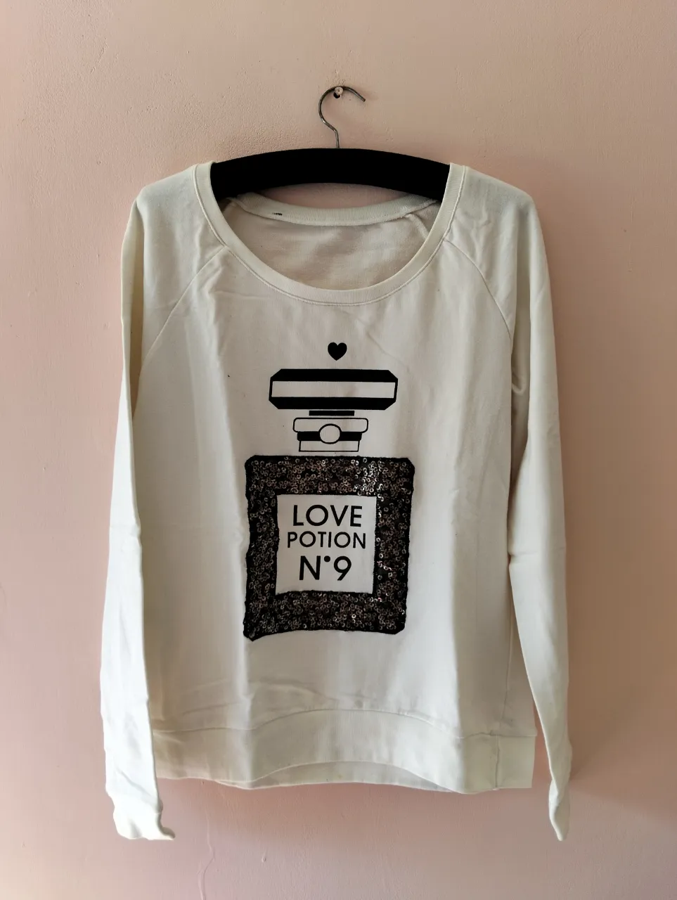 Buzo de cuello redondo para mujer, color blanco con estampado de perfume "Love Potion N°9" en lentejuelas negras. Ideal para un look casual y con onda.