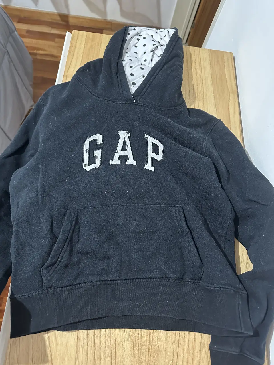 Buzo canguro negro de la marca GAP, con el logo de la marca en blanco en el frente. Tiene capucha con interior de lunares blancos y negros. Ideal para un look casual y cómodo. Es original, el precio es porque la tela ya está gastada (todo sano!! literal como se ve en la foto)
